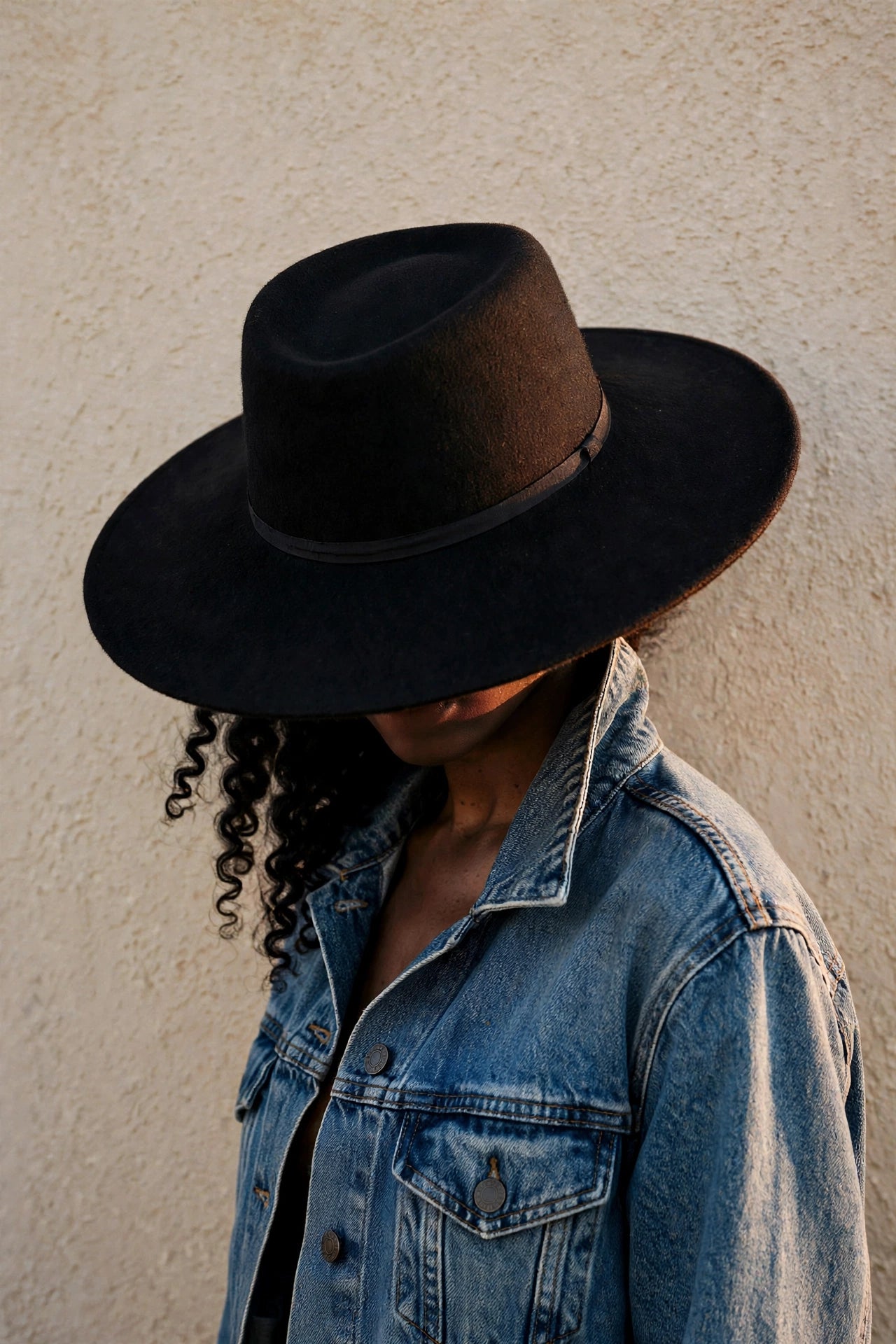 Black woman in a wide-brim black fedora and denim jacket