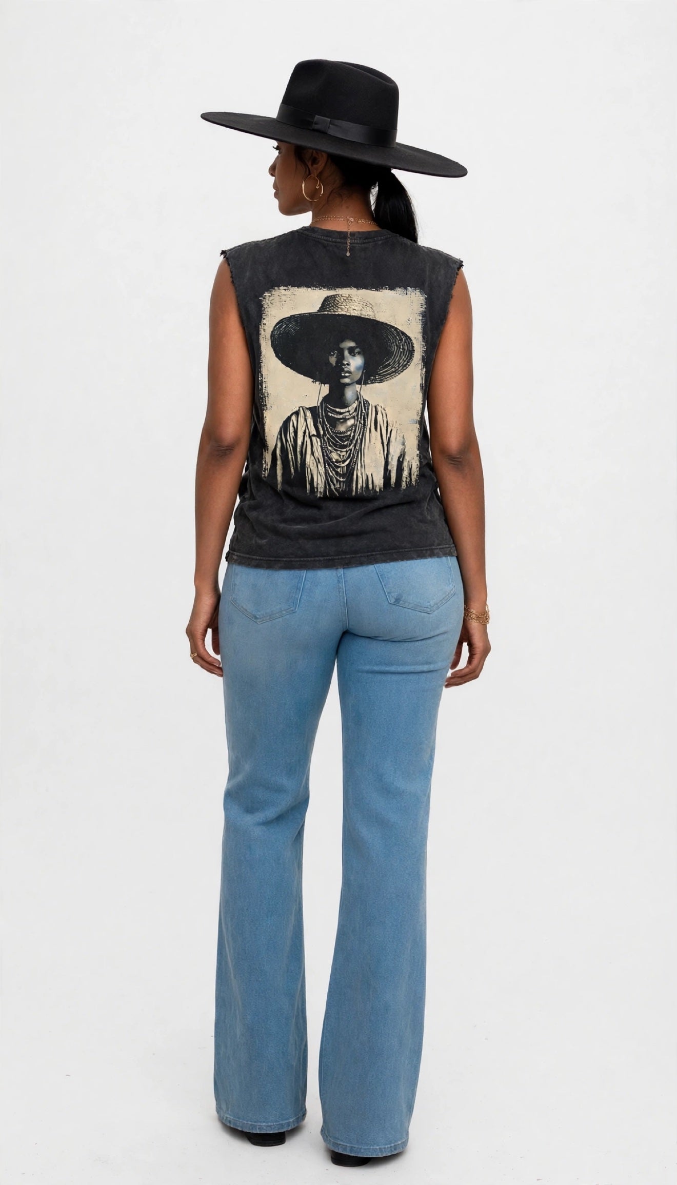 Back view of Erica in a black felt fedora modeling the black sleeveless cutoff tee with a large portrait graphic